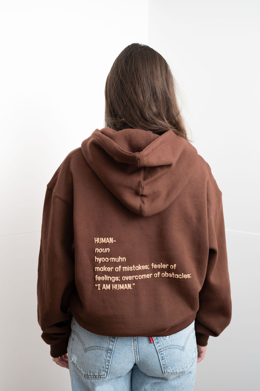 Back view of brown hoodie with the definition of human on the back. It reads Human - Noun- Hyoo-muhn - maker of mistakes; feeler of feelings; overcomer of obstacles "I am human"