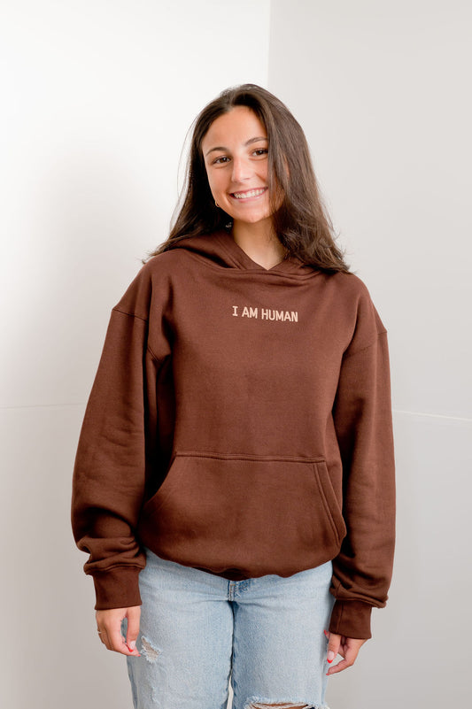 Front view of Elizabeth in brown human definition hoodie with the words I AM HUMAN written on the chest in tan lettering.