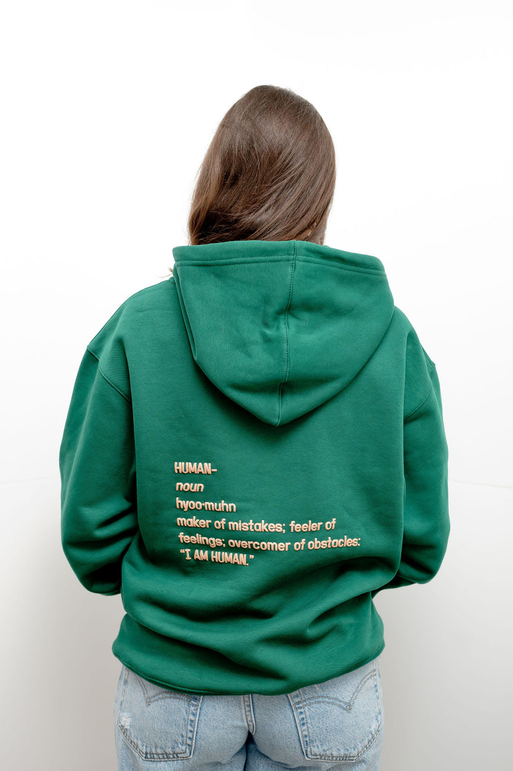 Back view of green hoodie with the definition of human on the back. It reads Human - Noun- Hyoo-muhn - maker of mistakes; feeler of feelings; overcomer of obstacles "I am human" 