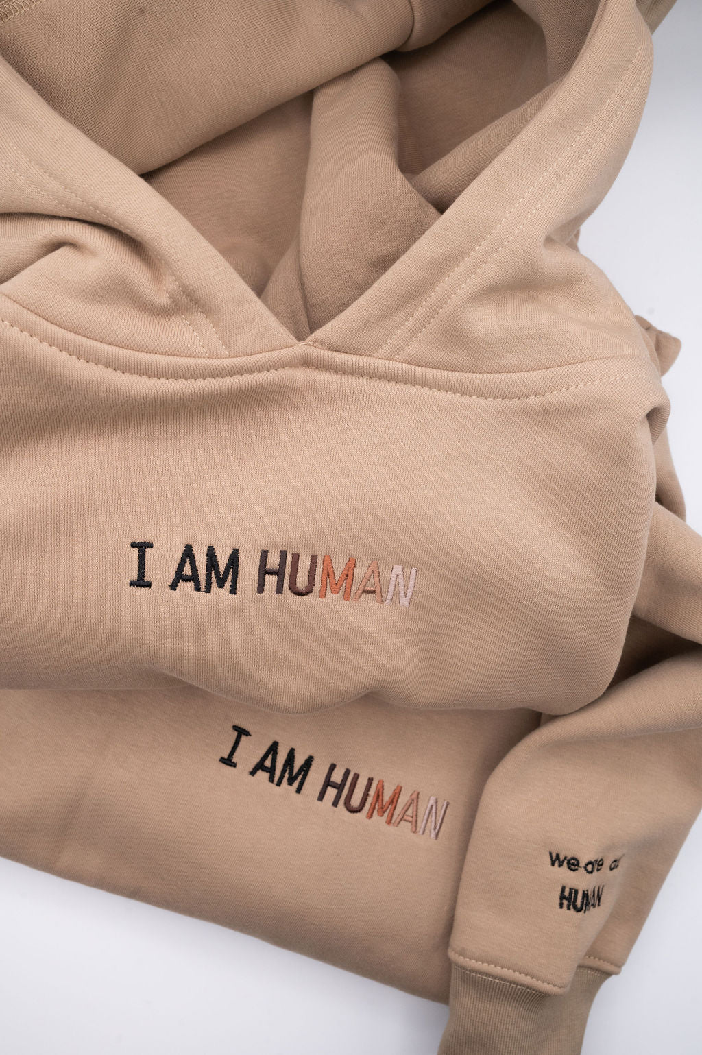 Close up of I AM HUMAN embroidered logo on chest and words 'we are all human' on sleeve. 